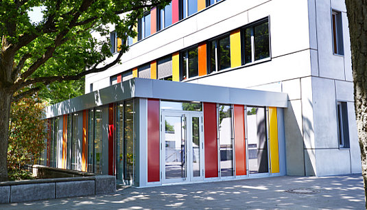 Schulbauerweiterung mit farbig verglasten Fassadenelementen passend zum Bestandsgebäude